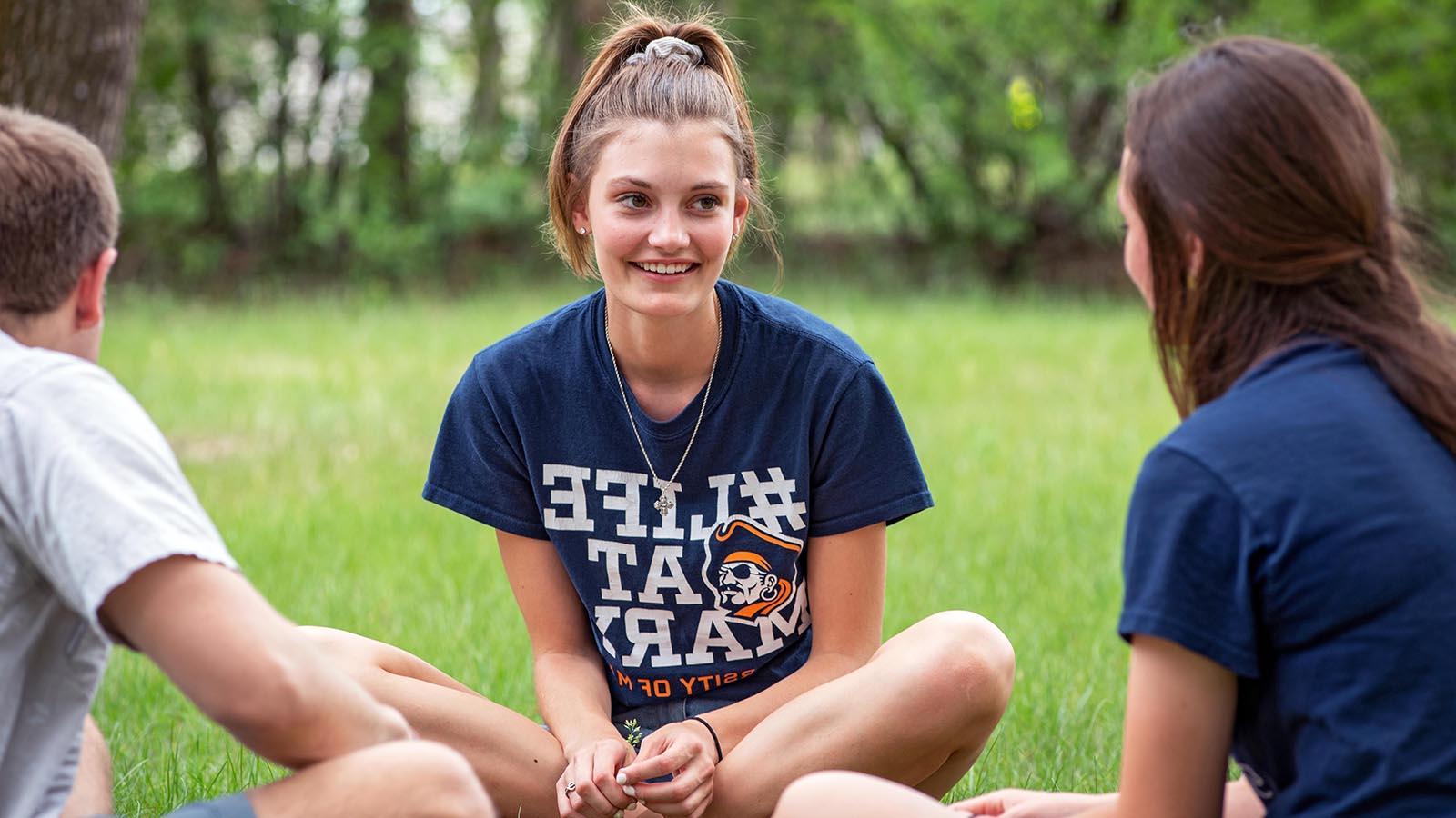 Three students sitting in the grass having a conversation.